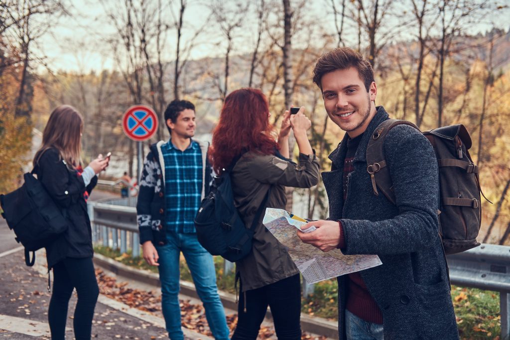 Group of young friends with backpacks sitting next to a road in forest